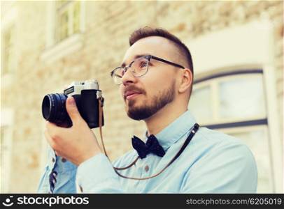 people, photography, technology, leisure and lifestyle - happy young hipster man with retro vintage film camera taking picture on city street