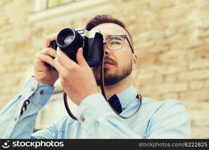 people, photography, technology, leisure and lifestyle - happy young hipster man with retro vintage film camera taking picture on city street