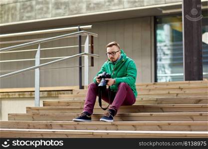 people, photography, technology, leisure and lifestyle - young hipster man holding digital camera with big lens and sitting on stairs in city