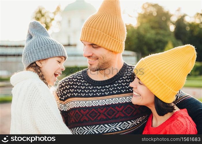 People, pleasant emotions and happiness concept. Happy young parents and their little adorble girl stand together, enjoy togetherness and calm atmosphere outdoors, feel relaxed, smile pleasantly