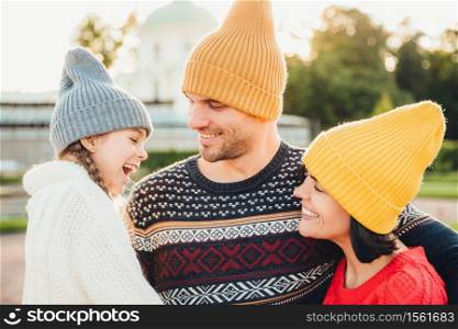 People, pleasant emotions and happiness concept. Happy young parents and their little adorble girl stand together, enjoy togetherness and calm atmosphere outdoors, feel relaxed, smile pleasantly