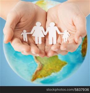 people, population, charity and life concept - close up of human hands holding paper family over earth globe and blue background