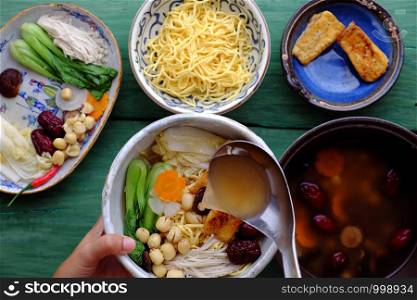 People prepare Vietnamese vegetarian homemade noodle soup bowl from vegan ingredient for breakfast, healthy dish from tofu, jujube fruit, lotus seed, bok choy, mushroom, spice, carrot