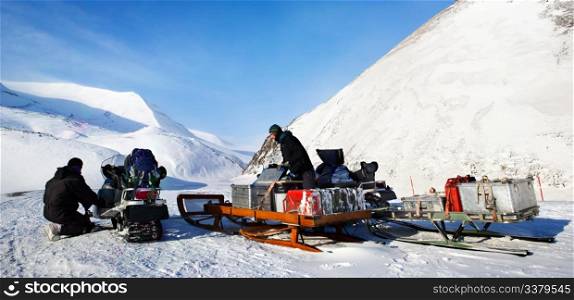 People preparing snowmobiles for an expedition through through winter conditions