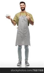 people, profession and job concept - happy smiling barista or waiter in apron holding cup of coffee and showing thumbs up over white background. barista or waiter with coffee showing thumbs up