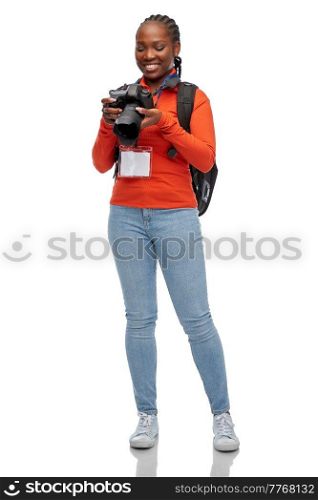 people, profession and photography concept - happy young woman or press photographer with digital camera, conference id card and backpack photographing over white background. woman photographer with camera and conference id