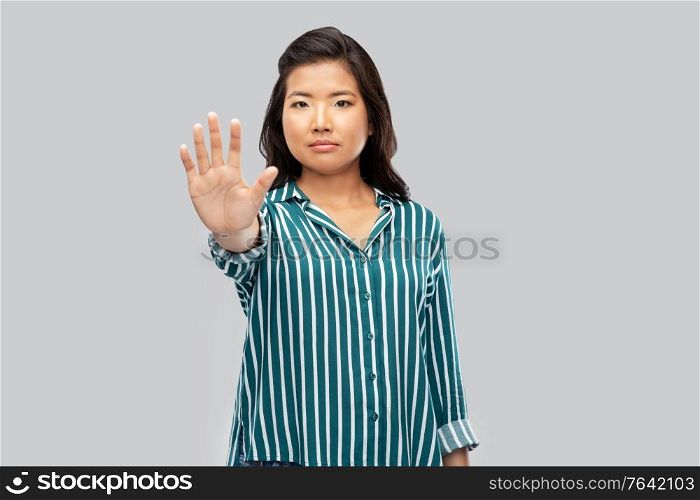 people, prohibition and rejection concept - asian young woman showing stop gesture over grey background. asian young woman showing stop gesture over grey