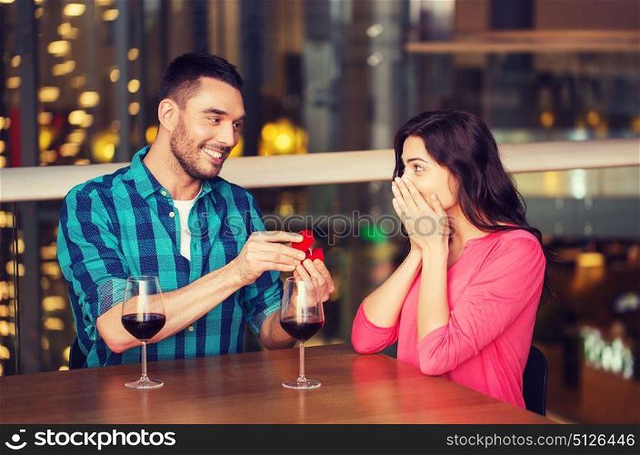people, proposal, love, couple and holidays concept - smiling man giving diamond engagement ring to his happy girlfriend at restaurant. man giving engagement ring to woman at restaurant
