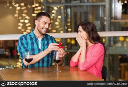 people, proposal, love, couple and holidays concept - smiling man giving diamond engagement ring to his happy girlfriend at restaurant