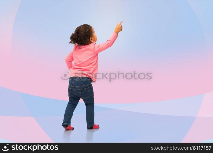 people, race, ethnicity and childhood concept - happy african american baby girl pointing finger to something from back over pink and violet background
