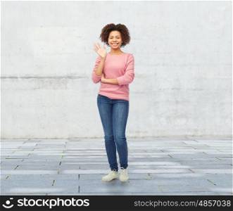 people, race, ethnicity and gesture concept - happy african american young woman waving hand over stone wall background
