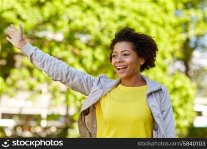 people, race, ethnicity and gesture concept - happy african american young woman waving hand in summer park