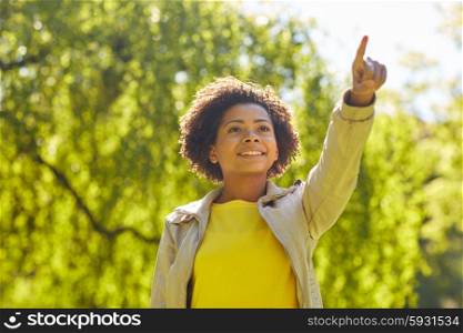 people, race, ethnicity and gesture concept - happy african american young woman pointing finger in summer park