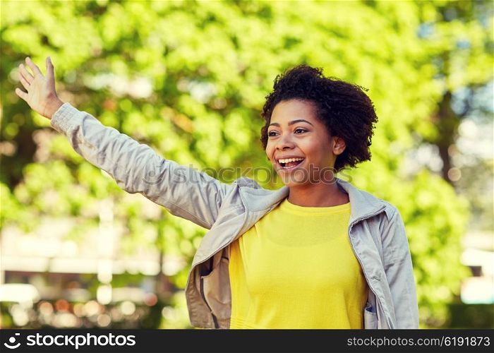 people, race, ethnicity and gesture concept - happy african american young woman waving hand in summer park