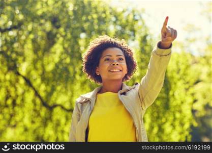 people, race, ethnicity and gesture concept - happy african american young woman pointing finger in summer park