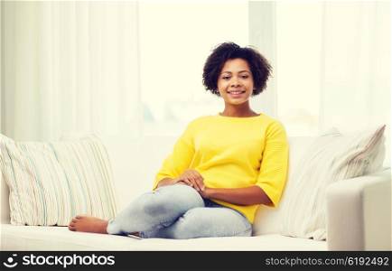 people, race, ethnicity and leisure concept - happy african american young woman sitting on sofa at home