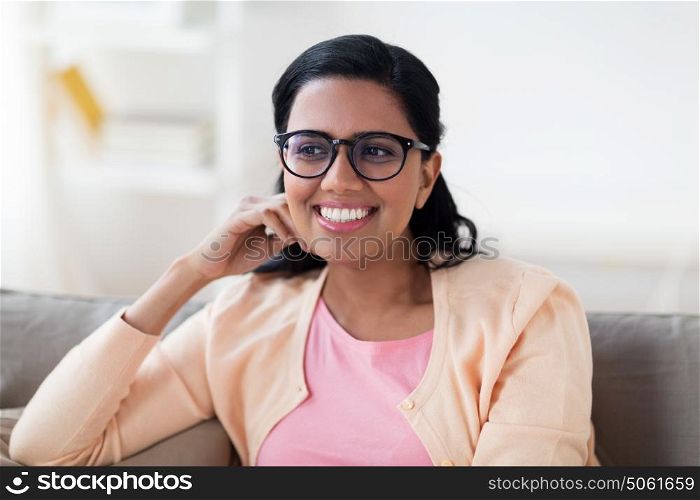 people, race, ethnicity and leisure concept - happy smiling young indian woman in glasses sitting on sofa at home. happy smiling young woman sitting on sofa at home