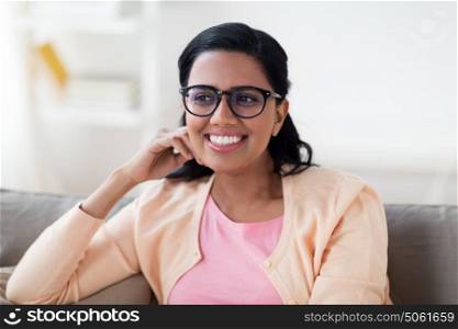 people, race, ethnicity and leisure concept - happy smiling young indian woman in glasses sitting on sofa at home. happy smiling young woman sitting on sofa at home