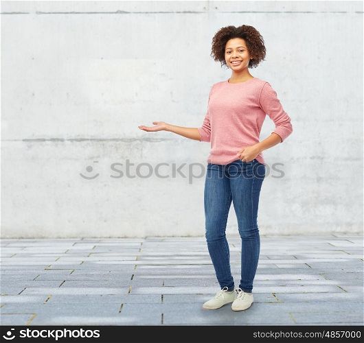 people, race, ethnicity and portrait concept - happy african american young woman holding something imaginary on hand over stone wall background