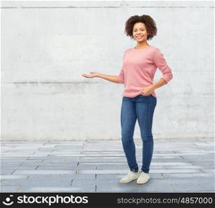 people, race, ethnicity and portrait concept - happy african american young woman holding something imaginary on hand over stone wall background