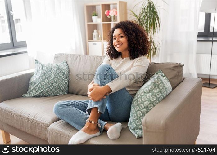 people, race, ethnicity and portrait concept - happy african american young woman sitting on sofa at home. happy african american young woman at home