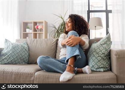 people, race, ethnicity and portrait concept - happy african american young woman sitting on sofa at home. happy african american young woman at home