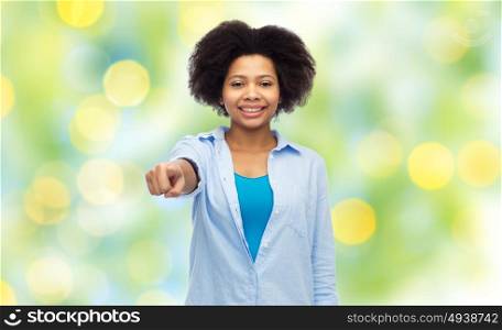 people, race, ethnicity, gesture and choice concept - happy african american young woman pointing finger to you over summer green lights background. happy african woman pointing finger to you