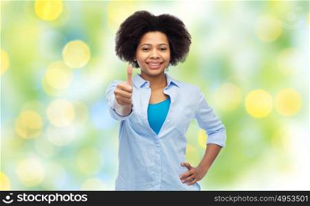 people, race, ethnicity, gesture and portrait concept - happy african american young woman showing thumbs up over summer green lights background. happy african american woman showing thumbs up