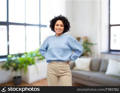 people, real estate and mortgage concept - happy smiling woman in blue sweater and jeans over home living room background. happy smiling woman in blue sweater at home
