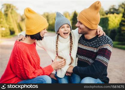 People, relationship and family concept. Smiling little girl with pigtails embrace her parents, express her positive emotions and feelings. Outdoor portrait of friendly family walk in beautiful park