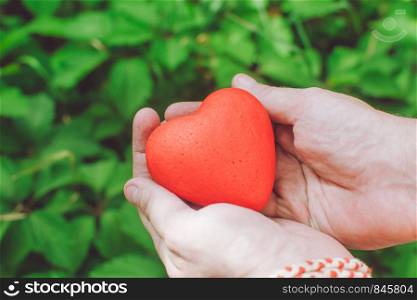 people, relationship and love concept - close up of mans hands holding red heart on green background. Mans hands holding red heart. Love concept