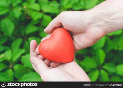 people, relationship and love concept - close up of mans hands holding red heart on green background. Love concept - close up of mans hands holding red heart