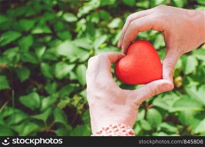 people, relationship and love concept - close up of mans hands holding red heart on green background. Relationship and love concept - close up of mans hands holding red heart
