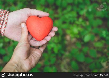 people, relationship and love concept - female and male hands holding red heart on green background. Relationship and love concept - female and male hands holding red heart
