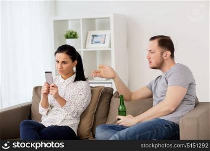 people, relationship difficulties and conflict concept - man drinking beer and woman with smartphone having argument at home. couple having argument at home