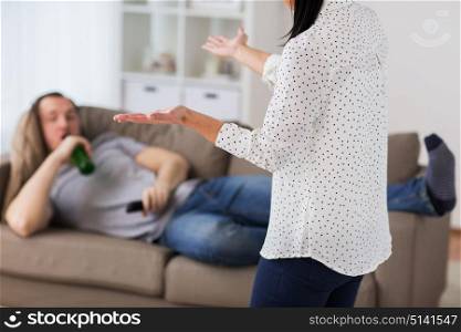 people, relationship difficulties, conflict and alcohol abuse concept - angry woman having argument with man drinking beer and watching tv at home. couple having argument at home
