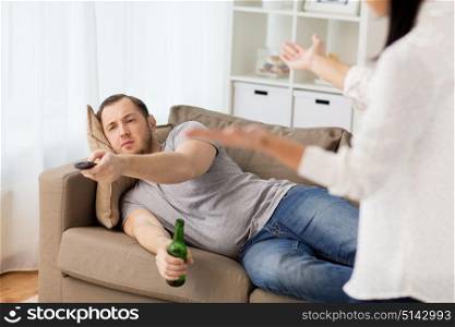 people, relationship difficulties, conflict and family concept - angry woman having agrument with man drinking beer and watching tv at home. couple having argument at home