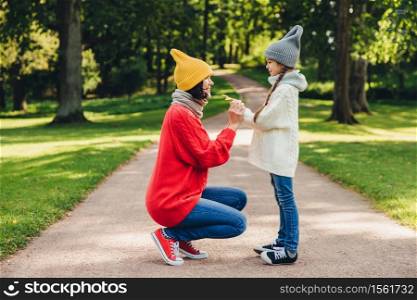 People, relationship, parenthood and childhood concept. Beautiful mother plays with her little daughter in park, gives yellow leaf, have sincere emotions and feeling or love to her lovely daughter