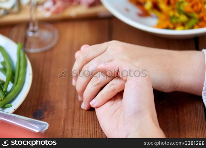 people, relationships and eating concept - hands of people sitting at table with food and praying before meal. hands of people at table praying before meal