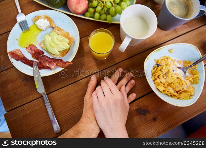 people, relationships and eating concept - multiracial couple holding hands while having breakfast at table full of food. couple hands on table full of food