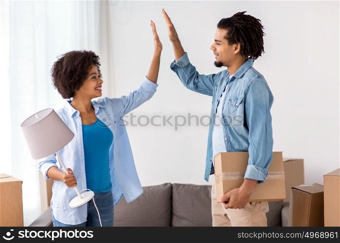 people, repair and real estate concept - smiling couple with cardboard boxes and lamp moving in or out of home and making high five. happy couple with stuff moving to new home
