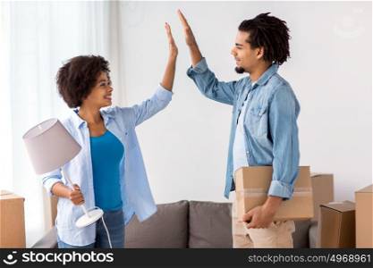 people, repair and real estate concept - smiling couple with cardboard boxes and lamp moving in or out of home and making high five. happy couple with stuff moving to new home
