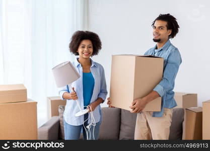 people, repair and real estate concept - smiling couple with cardboard boxes and lamp moving in or out of home. happy couple with stuff moving to new home