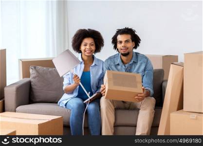 people, repair and real estate concept - smiling couple with cardboard boxes and lamp moving in or out of home. happy couple with stuff moving to new home