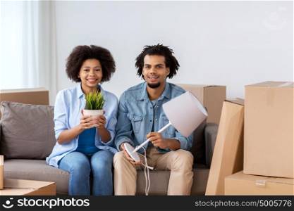 people, repair and real estate concept - smiling couple with cardboard boxes, plant and lamp moving in or out of home. happy couple with stuff moving to new home