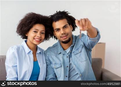people, repair and real estate concept - smiling couple with key and cardboard boxes moving in or out of home. happy couple with key and boxes moving to new home