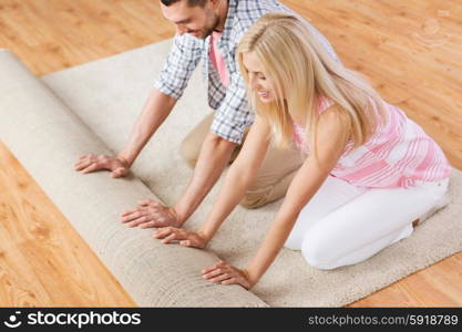 people, repair and renovation concept - happy couple unrolling carpet or rug on floor at home