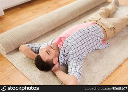 people, repair and renovation concept - happy man lying carpet or rug on floor at home