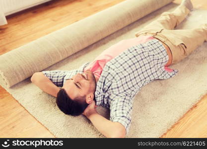 people, repair and renovation concept - happy man lying carpet or rug on floor at home