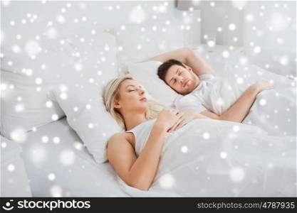 people, rest and relationships concept - happy couple sleeping in bed at home over snow